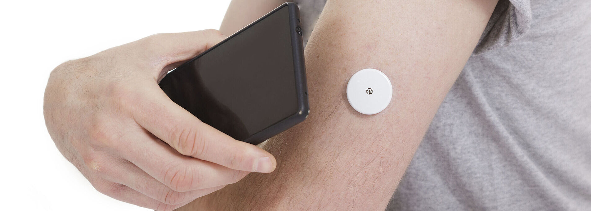 Ein schwarzes Smartphone wird an einen Arm mit Blutzuckermesser gehalten