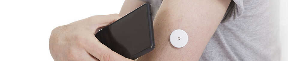 A black smartphone is held to an arm with a blood glucose meter