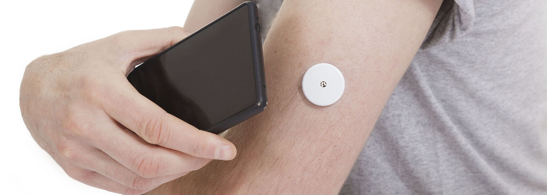 A black smartphone is held to an arm with a blood glucose meter