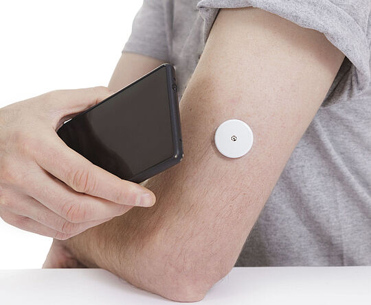 A black smartphone is held to an arm with a blood glucose meter