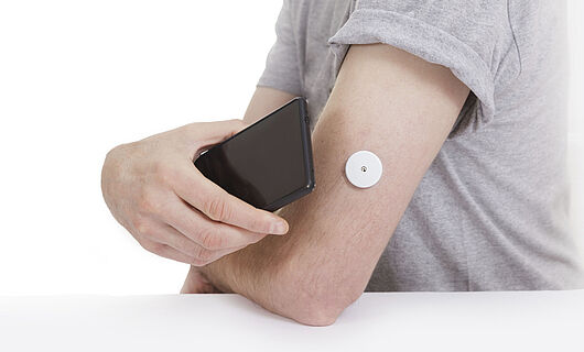 A black smartphone is held to an arm with a blood glucose meter