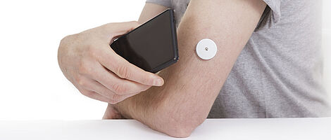 A black smartphone is held to an arm with a blood glucose meter