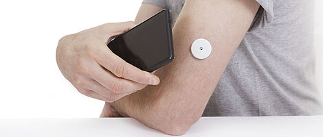 A black smartphone is held to an arm with a blood glucose meter