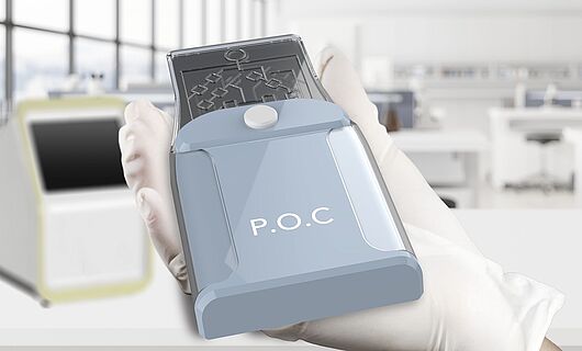 POC device in a hand with a glove, in the background a laboratory with a large window front