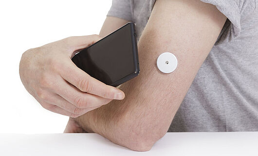 A black smartphone is held to an arm with a blood glucose meter