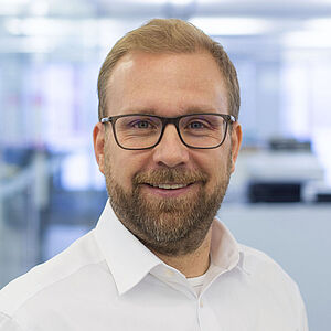 Lächelnder Mann in einem weißen Hemd. In einem gut beleuchteten Büro.