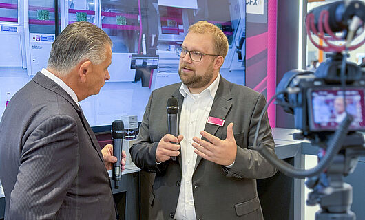 Two men in an interview in front of a running camera