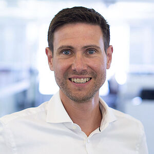 Smiling man in a white shirt standing in a brightly lit office.